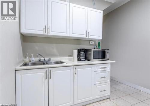 Kitchenette with white cabinetry, a double stainless steel sink, and light-colored countertops - 833 King Street E, Hamilton, ON 