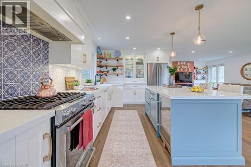 Gourmet kitchen featuring a patterned tile range backsplash, stainless steel range with hood, white perimeter cabinetry, light blue accent island, and wood-finish flooring - 1486 Augustine Drive, Burlington, ON - Indoor Photo Showing Kitchen With Upgraded Kitchen