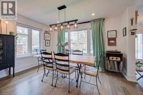 Wood-finish flooring throughout, featuring a multi-pane window with white trim, a linear pendant light fixture with clear glass shades, recessed ceiling lighting, and crisp white baseboards - 1486 Augustine Drive, Burlington, ON - Indoor Photo Showing Dining Room