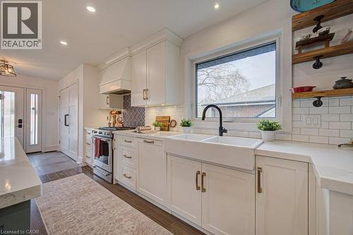 Contemporary kitchen featuring white shaker cabinetry, an integrated range hood, stainless steel appliances, a double basin farmhouse sink with a matte black faucet, and open wood shelving - 1486 Augustine Drive, Burlington, ON - Indoor Photo Showing Kitchen With Double Sink With Upgraded Kitchen