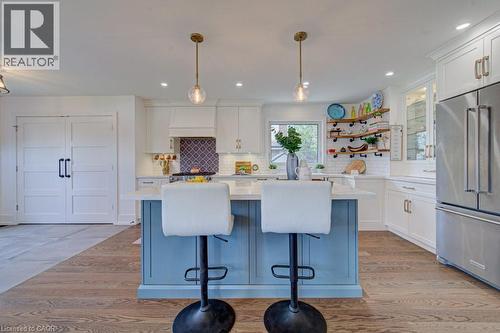 Kitchen featuring a blue-paneled island with seating, white shaker-style cabinetry, stainless steel appliances, and wood-finish flooring - 1486 Augustine Drive, Burlington, ON - Indoor Photo Showing Kitchen With Upgraded Kitchen