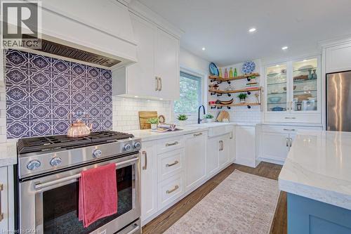 Kitchen featuring a stainless steel range with a decorative tile backsplash, complemented by white cabinetry with gold hardware - 1486 Augustine Drive, Burlington, ON - Indoor Photo Showing Kitchen