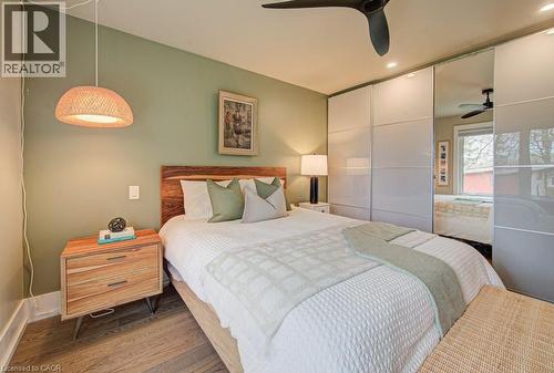 Wood-finish flooring anchors this room, featuring a wood headboard and a built-in wardrobe with mirrored and opaque sliding doors - 1486 Augustine Drive, Burlington, ON - Indoor Photo Showing Bedroom