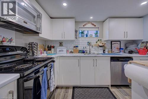 Kitchen featuring white cabinetry, subway tile backsplash, recessed lighting, wood-finish flooring, and a stainless steel dishwasher - 1486 Augustine Drive, Burlington, ON - Indoor Photo Showing Kitchen