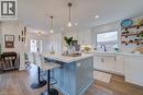 Kitchen featuring a central island with a light blue base and a light-toned countertop, white cabinetry with dark hardware, a white farmhouse sink with a black gooseneck faucet, and wood-finish floori - 1486 Augustine Drive, Burlington, ON  - Indoor Photo Showing Kitchen With Upgraded Kitchen 