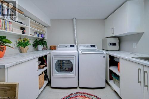 Dedicated utility space featuring a washer and dryer, extensive countertop space with a marble-finish surface, white cabinetry, open shelving, and an integrated sink basin - 1486 Augustine Drive, Burlington, ON - Indoor Photo Showing Laundry Room