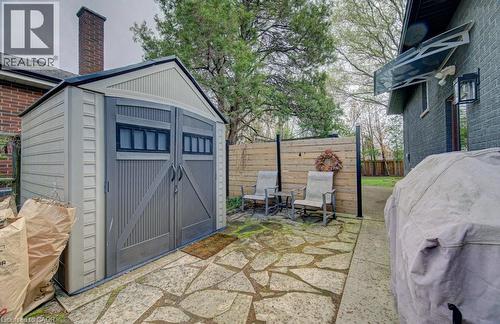 Compact storage shed with double doors and window accents, set on a natural stone patio - 1486 Augustine Drive, Burlington, ON - Outdoor With Exterior