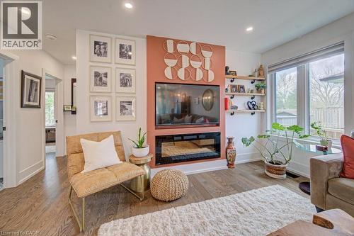 Open-concept living area featuring wood-finish flooring, a contemporary electric fireplace, and a large picture window - 1486 Augustine Drive, Burlington, ON - Indoor Photo Showing Living Room With Fireplace