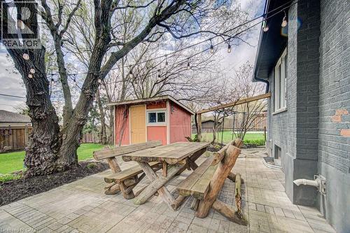 Expansive paver patio featuring a mature tree, string lighting, and a red storage shed with a yellow door - 1486 Augustine Drive, Burlington, ON - Outdoor