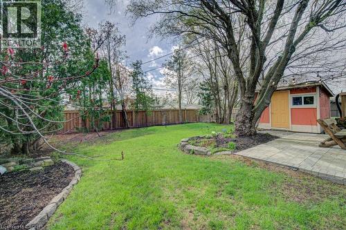 Expansive grassy yard featuring a wood privacy fence, mature trees, a paved patio area, and a vibrant storage shed - 1486 Augustine Drive, Burlington, ON - Outdoor
