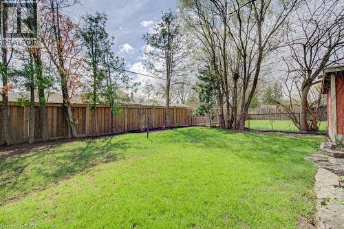 Spacious backyard featuring a manicured lawn, established perimeter trees, a full privacy fence, and natural stone hardscaping - 1486 Augustine Drive, Burlington, ON - Outdoor With Backyard