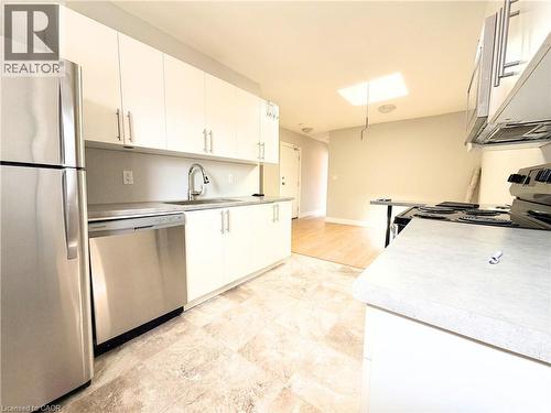Contemporary kitchen featuring abundant white cabinetry, stainless steel appliances, a stainless steel sink with a gooseneck faucet, light-toned countertops, and tiled flooring - 310 Barton Street E Unit# A, Hamilton, ON - Indoor Photo Showing Kitchen With Stainless Steel Kitchen