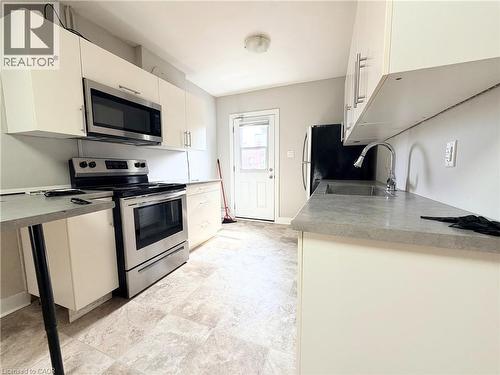 Galley kitchen featuring white cabinetry, stainless steel appliances including a range and microwave, light-toned countertop surfaces, and patterned tile-finish flooring - 310 Barton Street E Unit# A, Hamilton, ON - Indoor Photo Showing Kitchen With Stainless Steel Kitchen