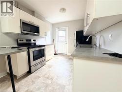 Galley kitchen featuring white cabinetry, stainless steel appliances including a range and microwave, light-toned countertop surfaces, and patterned tile-finish flooring - 