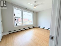 Bright room featuring a wide window, wood-finish flooring, a ceiling fan with integrated lighting, and baseboard heating - 