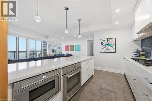 Modern kitchen featuring a large island with integrated stainless steel appliances, white cabinetry with chrome hardware, and a tile backsplash - 2060 Lakeshore Road Unit# 1501, Burlington, ON - Indoor Photo Showing Kitchen With Upgraded Kitchen