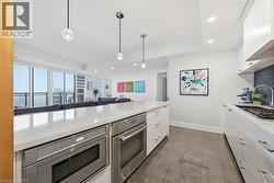 Modern kitchen featuring a large island with integrated stainless steel appliances, white cabinetry with chrome hardware, and a tile backsplash - 