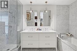 Marble-clad bathroom featuring a dual vanity, frameless glass shower enclosure, built-in bathtub, and recessed shower niche - 