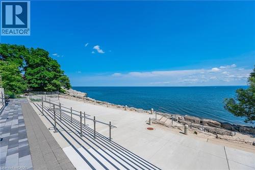 Waterfront paved promenade featuring a concrete surface with integrated metal handrails and a stone retaining wall - 2060 Lakeshore Road Unit# 1501, Burlington, ON - Outdoor With Body Of Water With View