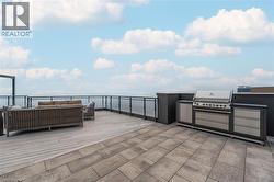 Spacious rooftop deck featuring a built-in outdoor kitchen with stainless steel appliances, a large paved patio area, and glass panel railing - 