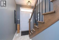 Foyer featuring a two-panel entry door with transom window, tile flooring, contemporary ceiling light fixture, and wood-finish staircase with black iron spindles - 