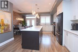 Open-concept kitchen and dining area featuring wood-finish flooring, a large kitchen island with seating, white cabinetry, black stainless steel appliances, and a brick accent wall in the dining space - 