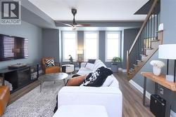 Open-concept living area featuring wood-finish flooring, a contemporary ceiling fan, and a wood staircase with black metal balusters - 