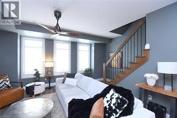 Living area featuring wood-finish flooring, a contemporary ceiling fan, and multiple windows with white plantation shutters - 