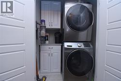 Dedicated laundry closet featuring a stacked washer and dryer, white paneled bifold doors, grey shaker-style cabinetry, and a light-toned countertop - 