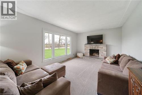 Living area featuring a stone-clad fireplace with hearth, a wall-mounted flat-screen television, and expansive windows - 2223 Hall Road, Binbrook, ON - Indoor Photo Showing Living Room With Fireplace