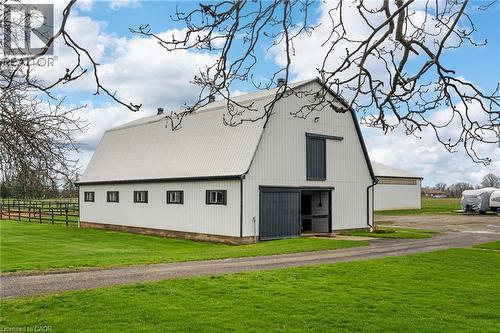 White barn structure with a gambrel roof and dark trim, featuring multiple windows and a large sliding barn door - 2223 Hall Road, Binbrook, ON - Outdoor