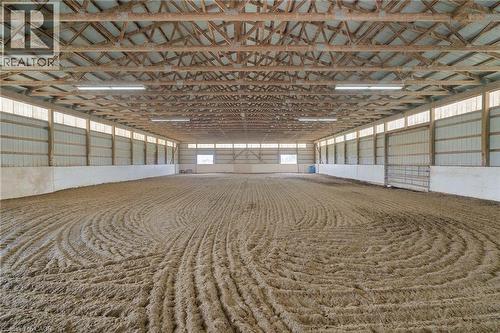 Spacious indoor arena featuring a prepared sand footing, exposed wood beam ceiling, ample overhead lighting, and perimeter translucent panels for natural illumination - 2223 Hall Road, Binbrook, ON - Indoor