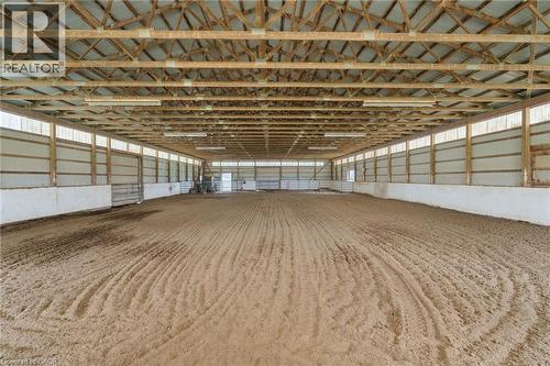 Spacious indoor arena featuring a sand riding surface, robust exposed wood beam ceiling, translucent wall panels for natural light, fluorescent overhead lighting, and white kickboards along the perime - 2223 Hall Road, Binbrook, ON - Indoor Photo Showing Other Room