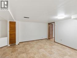 Spacious room featuring neutral-toned floor tile, white walls, and a warm wood-finish interior door - 