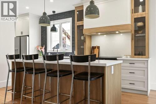 Kitchen featuring a central island with countertop seating, light wood-finish cabinetry, white upper cabinetry, and stainless steel appliances - 128 Canada Street, Hamilton, ON - Indoor