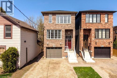Brick facade home featuring a single garage, a red front door, white trimmed windows, and a paved driveway - 128 Canada Street, Hamilton, ON - Outdoor