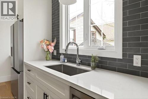 Kitchen featuring white cabinetry, a stainless steel sink with a gooseneck faucet, light-toned countertops, and a dark subway tile backsplash - 128 Canada Street, Hamilton, ON - Indoor Photo Showing Kitchen