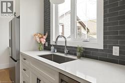 Kitchen featuring white cabinetry, a stainless steel sink with a gooseneck faucet, light-toned countertops, and a dark subway tile backsplash - 