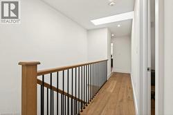 Hallway featuring wood-finish flooring, a contemporary wood and black metal baluster railing, recessed lighting, and a skylight - 