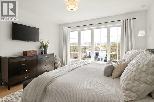 Expansive window wall with grid pattern, overhead flush mount light fixture, and wood-finish flooring - 128 Canada Street, Hamilton, ON - Indoor Photo Showing Bedroom