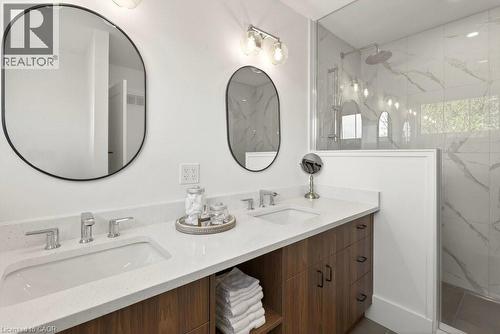 Bathroom featuring a dual-sink wood-finish vanity with stone-look countertops, chrome faucets, and two oval mirrors - 128 Canada Street, Hamilton, ON - Indoor Photo Showing Bathroom