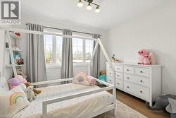 Bright room featuring multiple windows with natural light, wood-finish flooring, a white dresser with black hardware, and an overhead three-light fixture - 