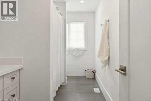 Bathroom featuring a white shower curtain, vanity with a white countertop and shaker-style cabinetry, a window with a white blind, and dark-toned floor tiles - 128 Canada Street, Hamilton, ON - Indoor Photo Showing Bathroom