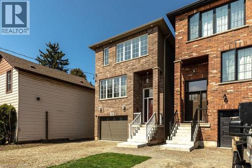 Brick exterior with multiple windows, an integrated garage, a covered entryway, and concrete steps with metal railings - 128 Canada Street, Hamilton, ON - Outdoor