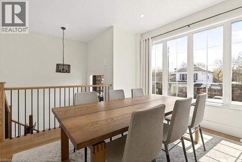 Bright dining area featuring expansive windows, wood-finish flooring, a contemporary pendant light fixture, and an open railing with metal balusters - 128 Canada Street, Hamilton, ON - Indoor Photo Showing Dining Room