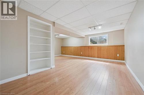 Spacious finished lower level featuring wood-finish flooring, built-in shelving, wood paneling, drop ceiling, and recessed window - 365 Pioneer Drive Unit# 25, Kitchener, ON - Indoor Photo Showing Other Room