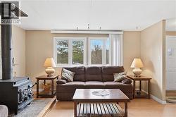 Living area featuring light wood-finish flooring, a black wood-burning stove, two large windows, a white paneled door, and neutral wall paint - 
