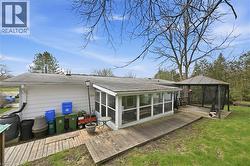 Exterior featuring a screened-in porch with multiple windows, a wood deck, and a detached gazebo with netting - 