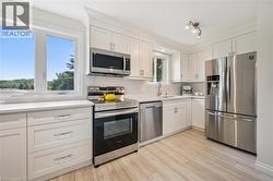 Kitchen featuring white cabinetry, stainless steel appliances, light-toned wood-finish flooring, white countertops, and a tile backsplash - 