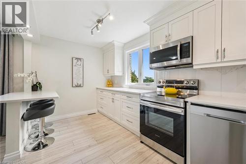 Bright kitchen featuring stainless steel appliances, white cabinetry, a built-in breakfast bar, recessed lighting, and wood-finish flooring - 97 Bechtel Drive, Kitchener, ON - Indoor Photo Showing Kitchen